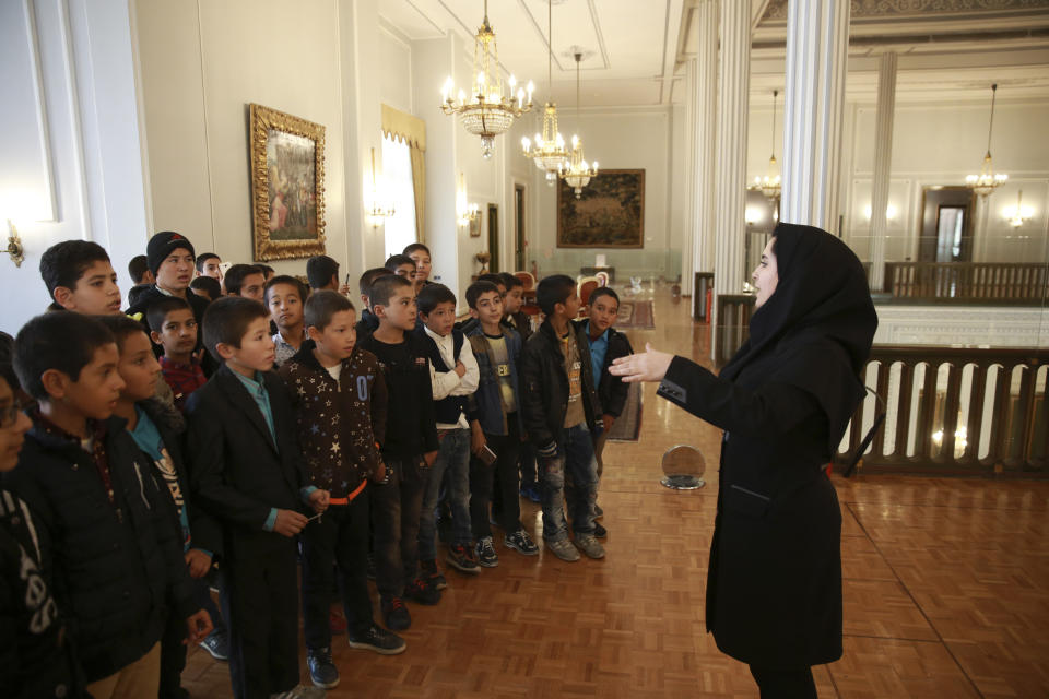 In this Tuesday, Jan. 15, 2019 photo, museum guide Zeinab Sadat Asadi explains for schoolboys as they visit Niavaran Palace, now a museum, that was the primary and last residence of late Shah Mohammad Reza Pahlavi and his family prior to leaving Iran for exile during the 1979 Islamic Revolution, in northern Tehran, Iran. The palace complex of mansions on a 27-acre plot, nestled against the Alborz Mountains, now welcomes the public to marvel at the luxuries the shah enjoyed as Iran's monarch for nearly four decades. It costs about $1 to enter. (AP Photo/Vahid Salemi)