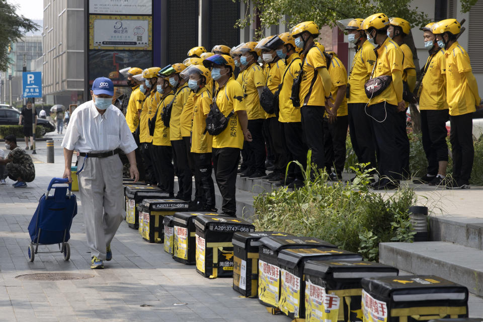 An elderly man wearing a mask to curb the spread of the coronavirus pulls along a shopping cart past delivery men gathered for a briefing before work in Beijing Thursday, July 23, 2020. (AP Photo/Ng Han Guan)