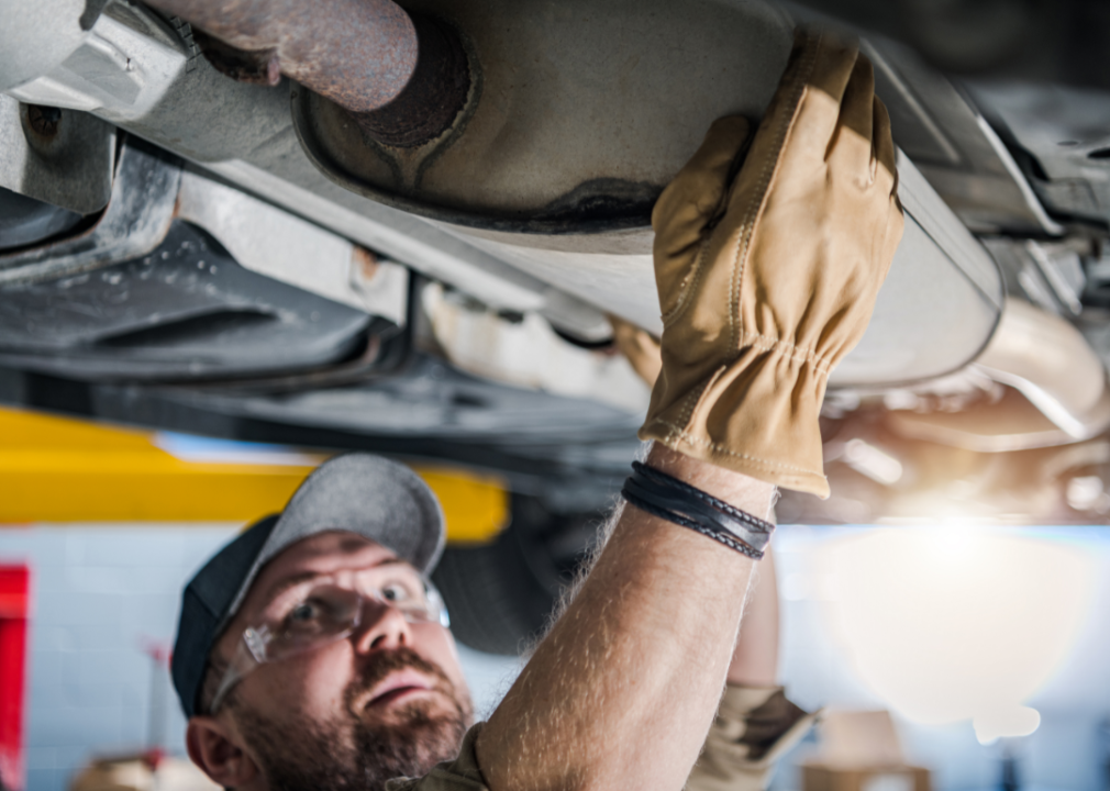 View of underside of car and mechanic checking on catalytic converter.