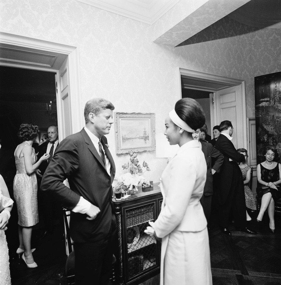 President John F. Kennedy visits with actor and singer Diahann Carroll. Eunice Kennedy Shriver stands at far left in background.