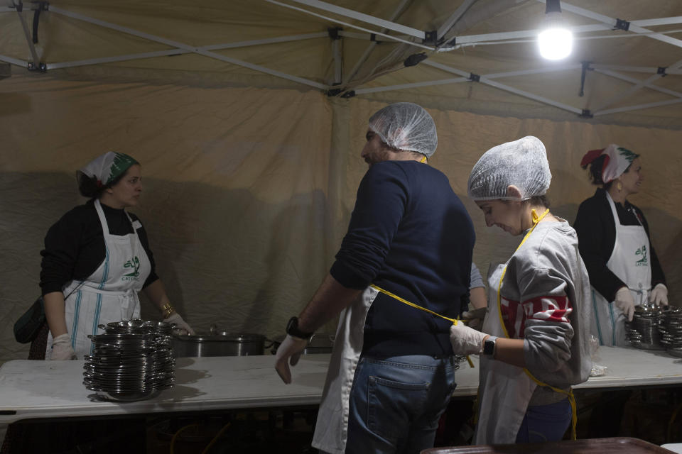 In this Monday, Dec. 23, 2019, photo, a woman ties an apron on a fellow volunteer before they serve a public Christmas dinner for the needy in Martyrs Square where anti-government activists are encamped in Beirut, Lebanon. Lebanon is entering its third month of protests, the economic pinch is hurting everyone, and the government is paralyzed. So people are resorting to what they've done in previous crises: They rely on each other, not the state. (AP Photo/Maya Alleruzzo)