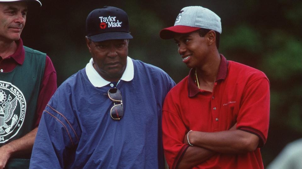 Earl Woods stands next to a smiling Tiger Woods on a golf course.