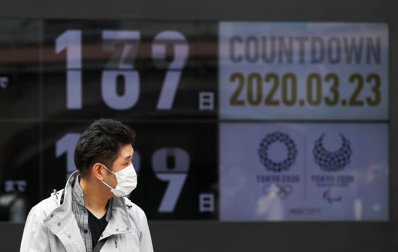 A passersby, wearing a face mask due to the outbreak of the coronavirus disease (COVID-19), walks past a screen counting down the days to the Tokyo 2020 Olympic Games