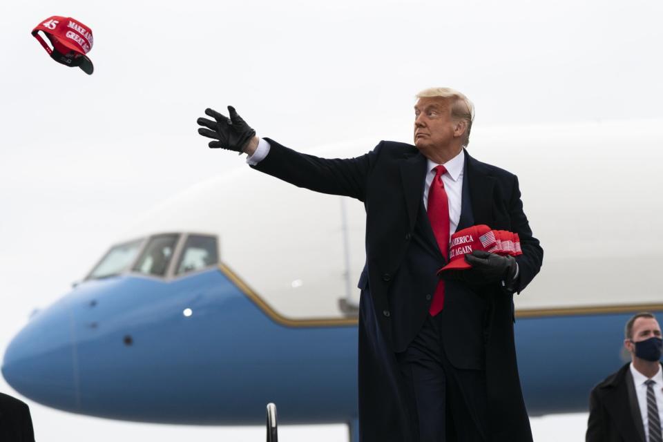 President Trump throws red MAGA hats to a rally crowd.