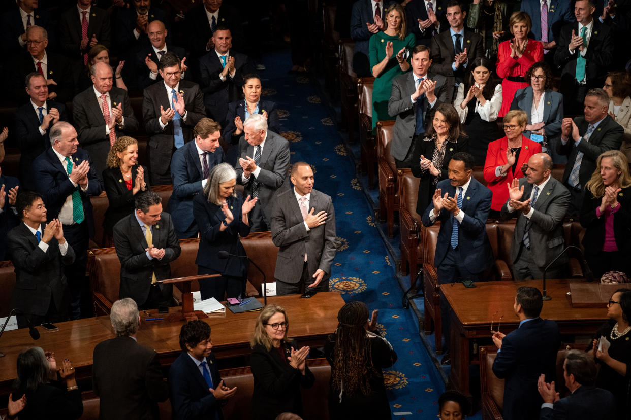 Members of the Democratic Party stand and clap for Rep. Hakeem Jeffries, who clasps his hand to his heart.