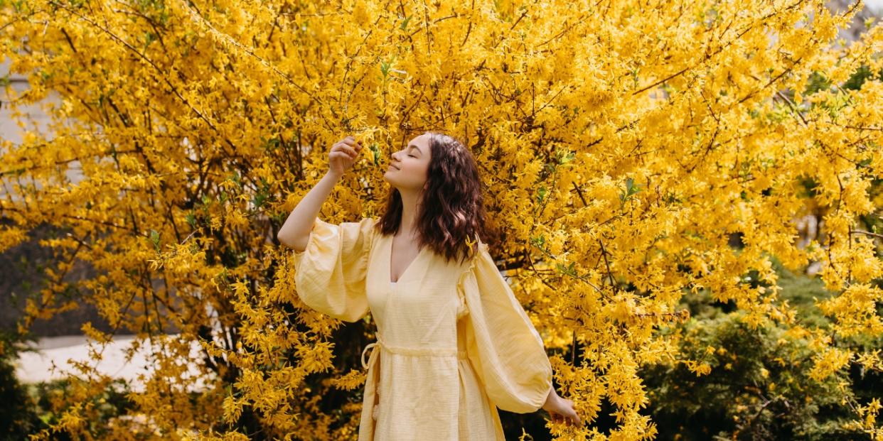 woman in yellow dress by forsythia flowers - mothering in a transitional season