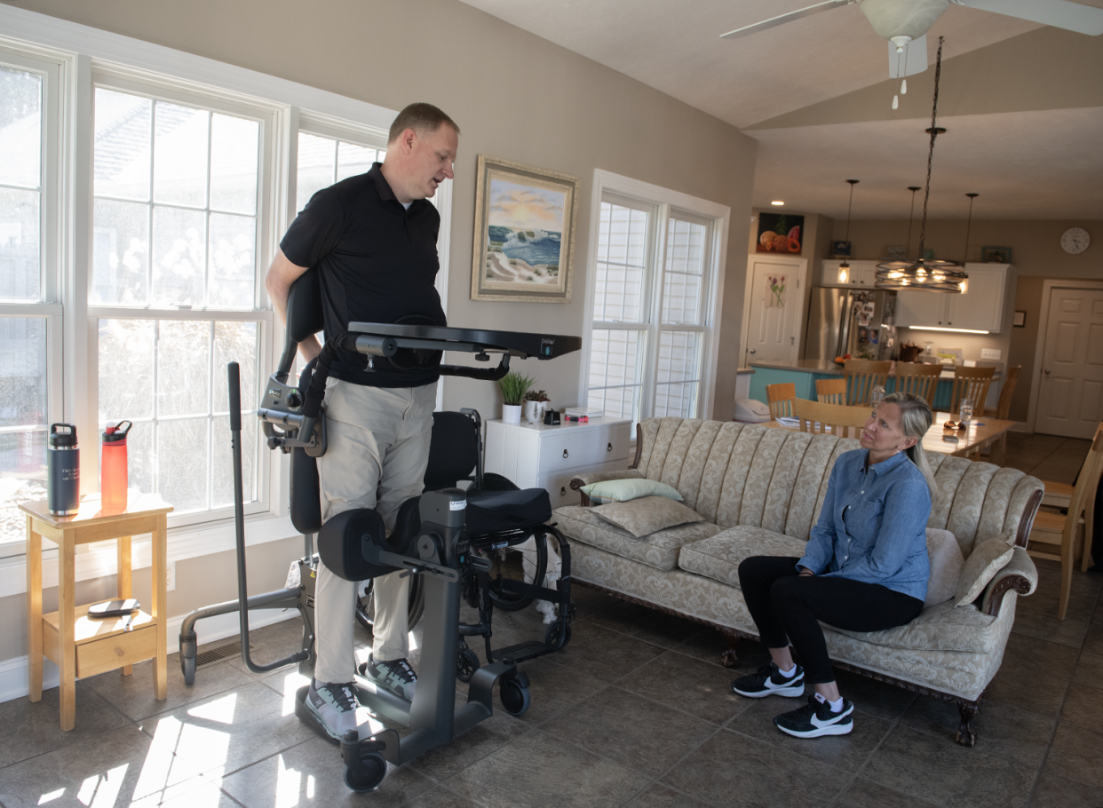 Jason Kolb, who is 6 feet, 5 inches tall, uses a standing frame while his wife Amy watches in their Kent home. Kolb was injured in a skiing accident last January.