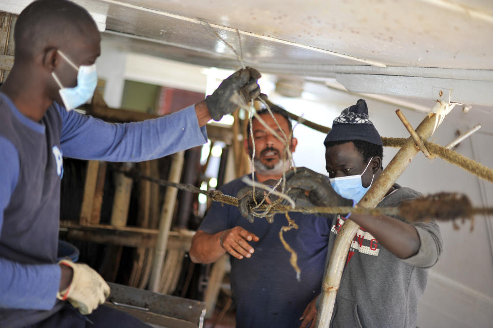 Waly Sarr, 30, right, Ibrahima Mbaye, 41, left, both from Senegal, and Salvatore Di Battista work on the deck of the "Vincenzo Padre" fishing boat where they work as fishermen, in the Island of Lampedusa, southern Italy, Thursday, May 13, 2021. The tiny island of Lampedusa, which is closer to Africa than the Italian mainland, is in the throes of yet another season of migrant arrivals, and Mbaye and Sarr can only watch from shore as their fellow African countrymen risk their lives to get here via smugglers' boats. (AP Photo/Salvatore Cavalli)