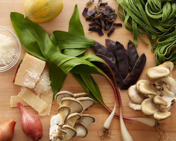 Vegetables, cheese, and pasta laid out on a wood countertop.