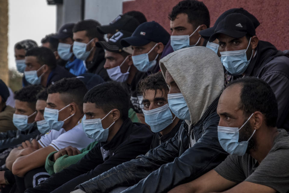 Migrants from Morocco sit after arriving at the coast of the Canary Island, crossing the Atlantic Ocean sailing on a wooden boat on Tuesday, Oct.20, 2020. Some 1,000 migrants have spent the night again sleeping in emergency tents in a dock while authorities in the Canary Islands complain that the Spanish government keeps blocking transfers of newly arrived migrants to the mainland over coronavirus concerns. (AP Photo/Javier Bauluz)