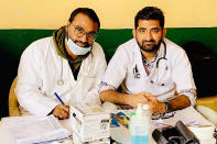 In this October 2019 photo provided by Bharat Sangwan, Joginder Chaudhary, left, and his friend and colleague Sangwan volunteer at a medical camp for women. After the virus killed the 27-year-old Chaudhary in late July 2020, his mother wept inconsolably. With her son gone, Premlata Chaudhary said, how could she go on living? Three weeks later, on Aug. 18, the virus took her life, too — yet another number in an unrelenting march toward a woeful milestone. (Courtesy of Bharat Sangwan via AP)