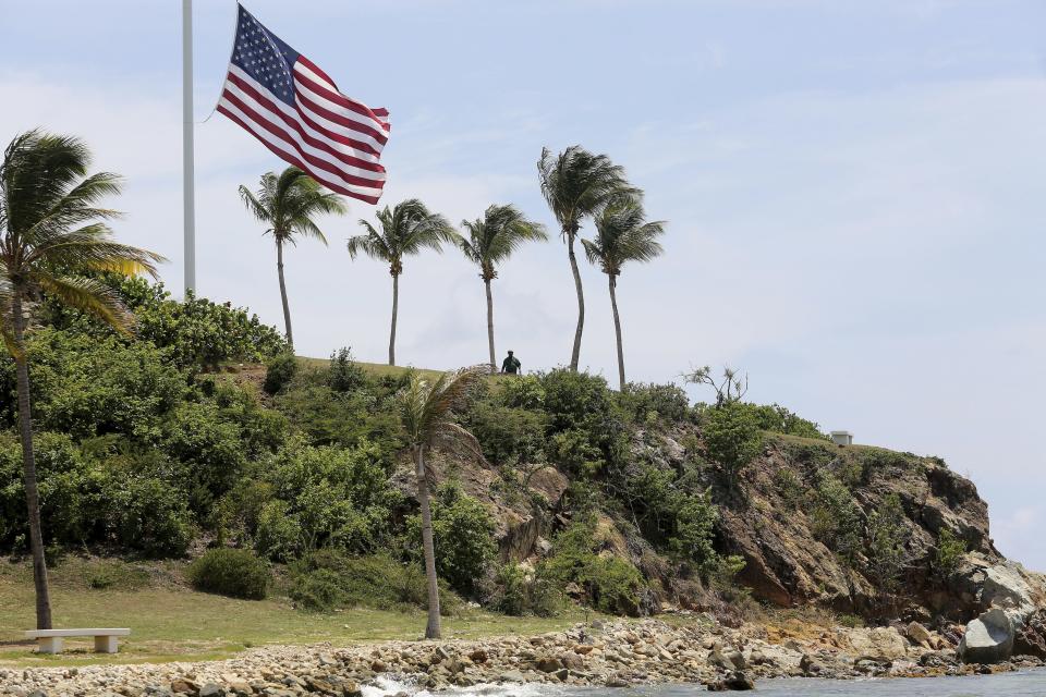 A man stands near a U.S. flag at half staff on Little St. James Island, in the U. S. Virgin Islands, a property owned by Jeffrey Epstein, Wednesday, Aug. 14, 2019. Tourists and locals alike are powering up boats to take a closer look at a place nicknamed “Pedophile Island’ that lies just off the southeast coast of St. Thomas. (AP Photo/Gabriel Lopez Albarran)