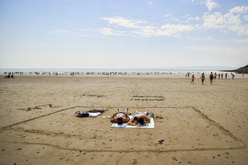 People sunbathe in a marked out square in the sand, indicating two meters, on Barry Island beach, in Wales, Friday, July 31, 2020. First Minister for Wales, Mark Drakeford, has announced that from Monday up to 30 people can meet outside while maintaining social distancing in the latest easing of coronavirus measures in Wales. (Ben Birchall/PAvia AP)