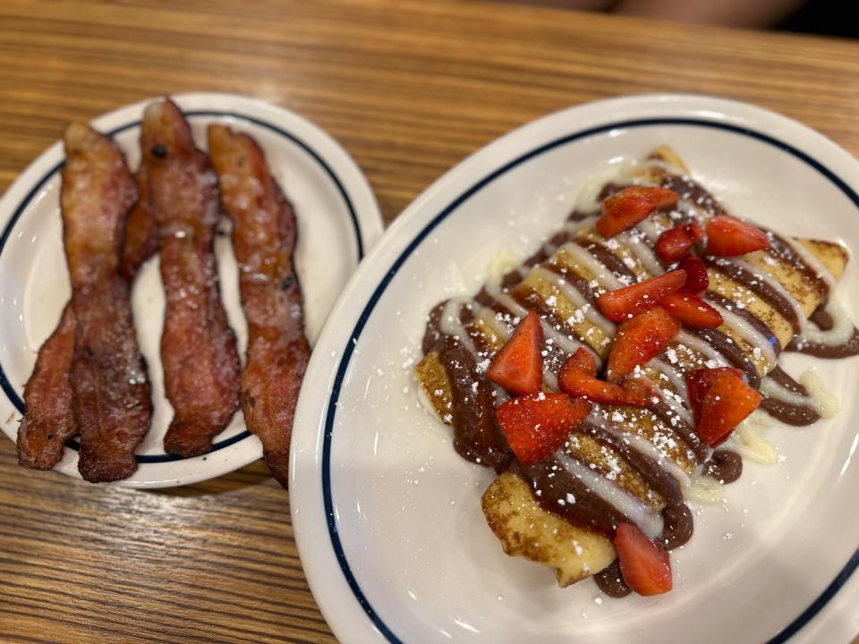 cinnamon bun crepes topped with strawberries on plate next to plate of bacon strips at ihop