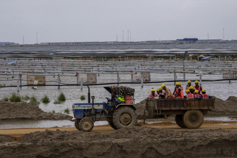 Workers sit on a tractor trailer as they make their way to work at the construction site of Adani Green Energy Limited's Renewable Energy Park in the salt desert of Karim Shahi village, near Khavda, Bhuj district near the India-Pakistan border in the western state of Gujarat, India, Thursday, Sept. 21, 2023. India is developing a 30 gigawatt hybrid — wind and solar — renewable energy project on one of the largest salt deserts in the world. (AP Photo/Rafiq Maqbool)