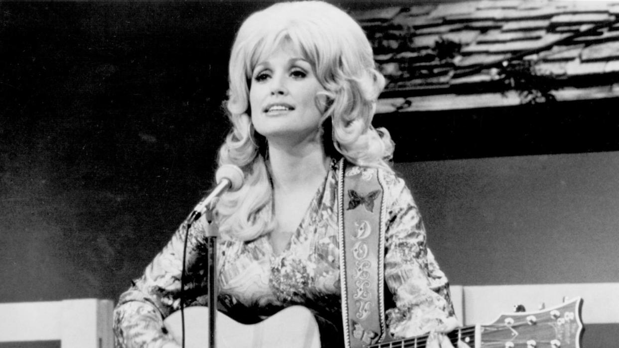 dolly parton playing guitar in front of a microphone and looking off into a crowd