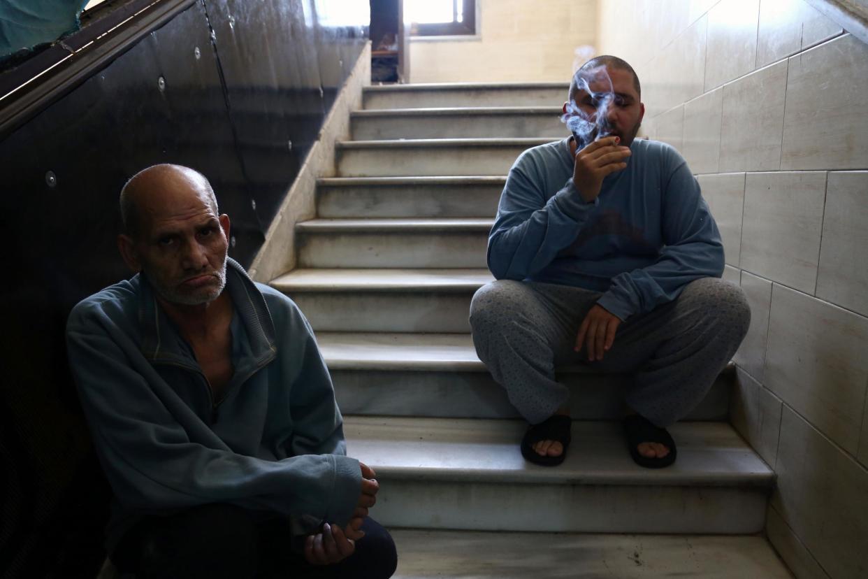 A Syrian patient smokes a cigarette as he sits on a staircase with another man at a mental health clinic - the sole such facility in the rebel-held north of Syria - in the town of Azaz, near the border with Turkey, on 6 July 2017: AFP