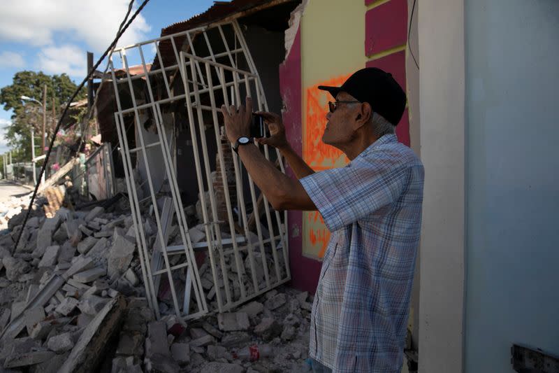 A man uses his phone to take photos of damaged houses after an earthquake in Guanica