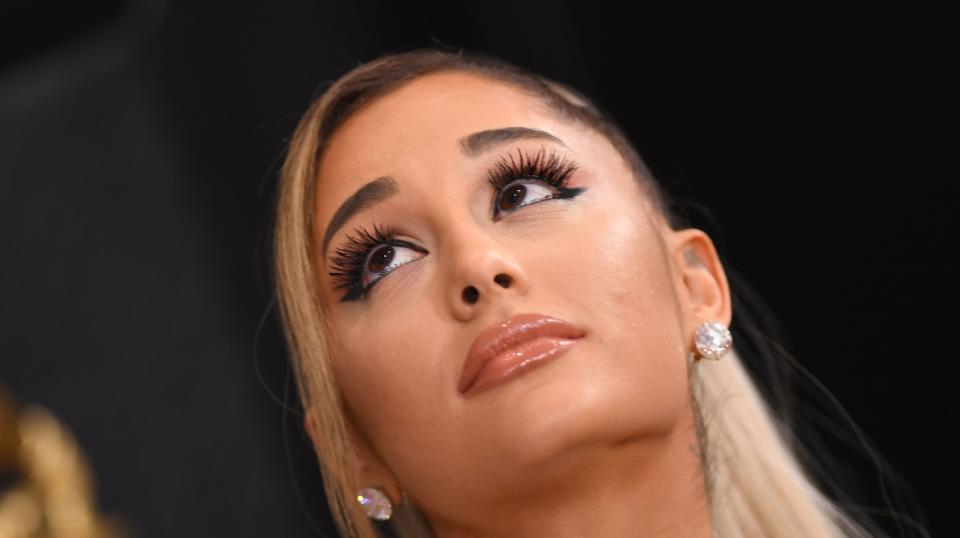 Ariana Grande looking upward with dramatic makeup and diamond earrings. She has long, straight hair partially pulled back