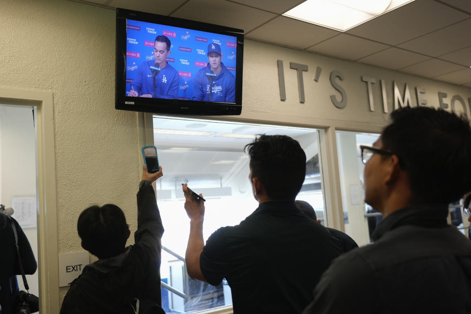 Reporters watch a video screen displaying Los Angeles Dodgers' Shohei Ohtani, right, and interpreter Will Ireton during a news conference at Dodger Stadium in Los Angeles, Monday, March 25, 2024. (AP Photo/Jae C. Hong)