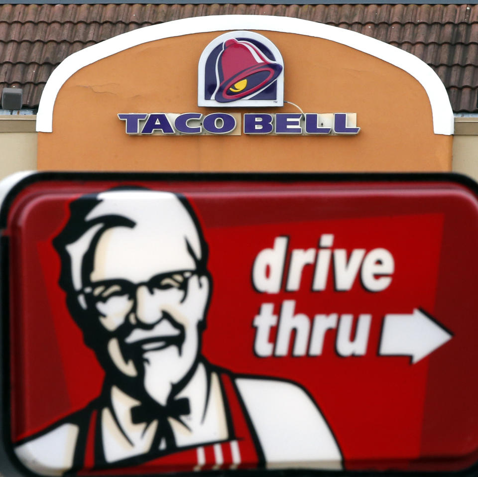 FILE - This Jan. 31, 2014, file photo, shows a Taco Bell facade behind a KFC drive-thru sign in Saugus, Mass.  The owner of KFC and Taco Bell, is teaming up with Grubhub to expand its delivery business. Yum Brands said Thursday, Feb. 8, 2018,  that Grubhub will run KFC and Taco Bell delivery and online ordering in the United States. GrubHub will provide delivery people and its technology.( (AP Photo/Elise Amendola, File)