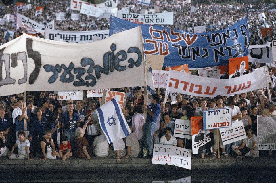 A crowd photo of protesters outside holding large cloth banners and some Israeli flags.