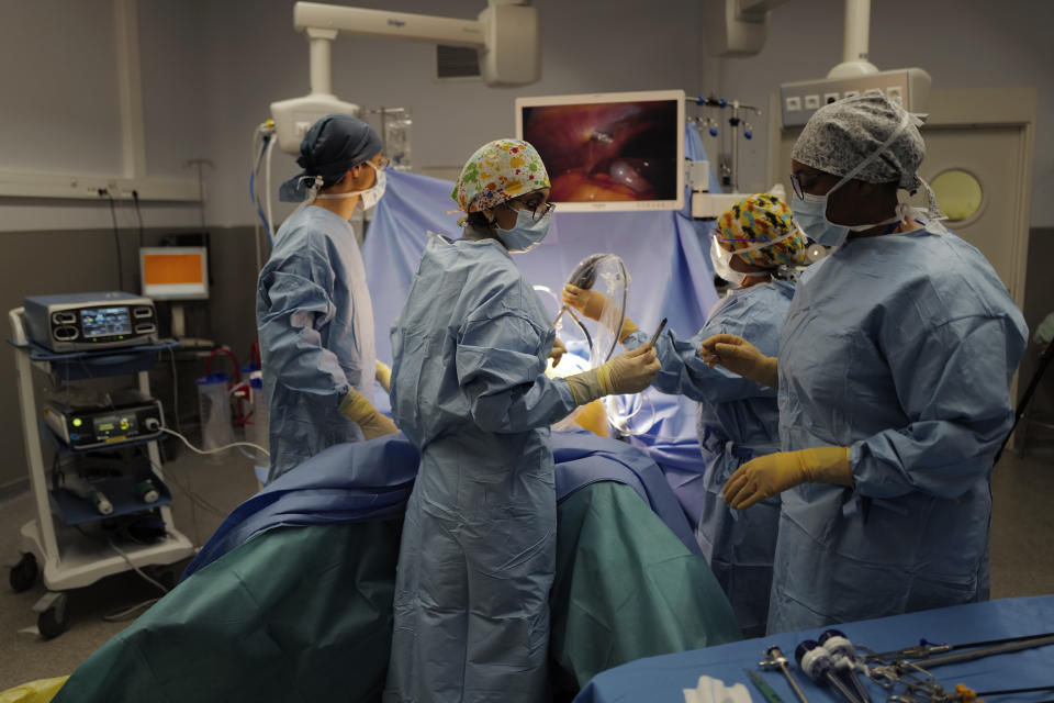 Surgeon Lara Ribeiro Parenti, second left, holds a surgical instrument during the surgery of Caroline Erganian at Bichat Hospital, AP-HP, in Paris, Wednesday, Dec. 2, 2020. Erganian, 58, hopes to shed more than a third of her weight as a result of having a large part of her stomach cut out and be free of knee and back pain — and of her cane. She prayed in the final weeks that her phone wouldn't ring with news of another delay. (AP Photo/Francois Mori)