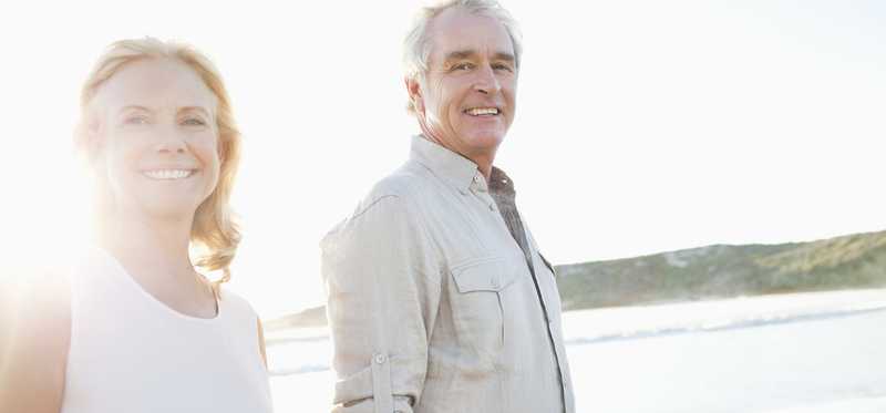An elderly couple walks on a beach.