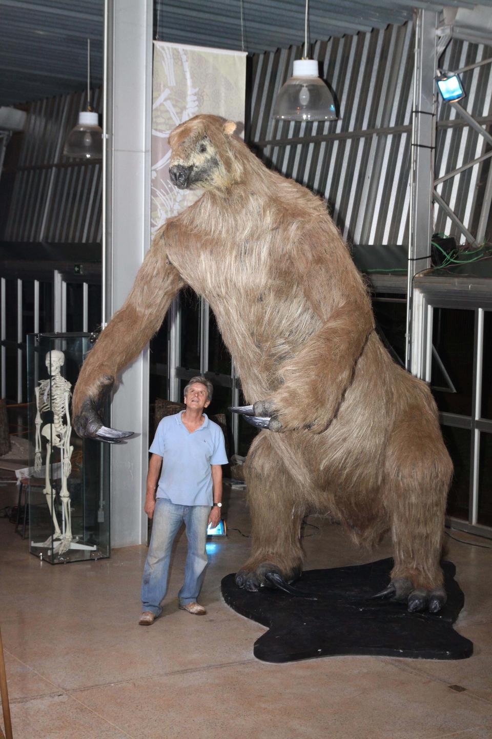 A man standing next to a model of a giant sloth