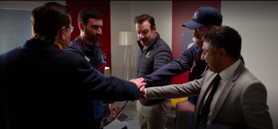 Ted, Leslie, and the other coaches with their hands together in "Ted Lasso."