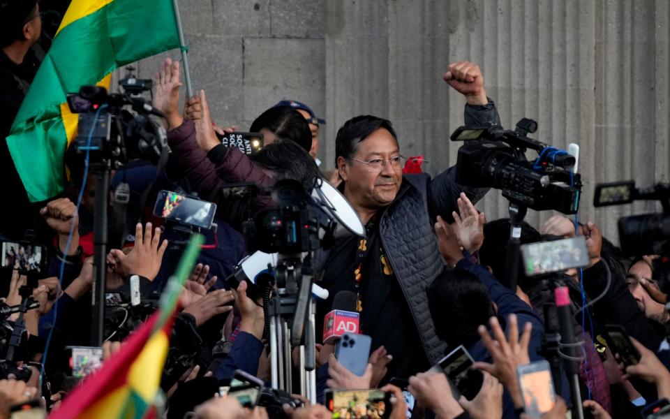 Bolivian president Luis Arce raises a clenched fist surrounded by supporters and media in La Paz