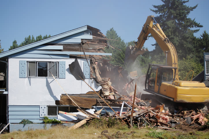 An excavator demolishing a white house.