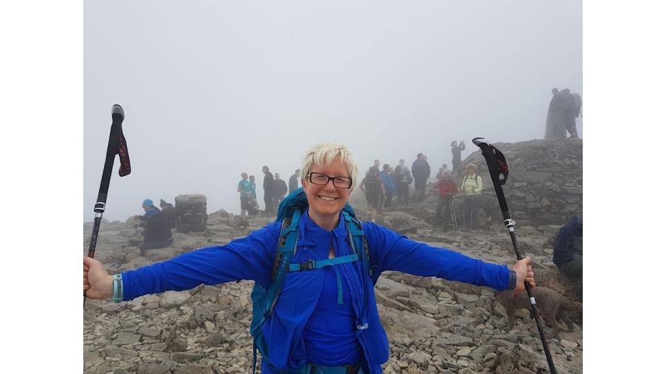 Woman in blue at the top of a mountain with walking poles