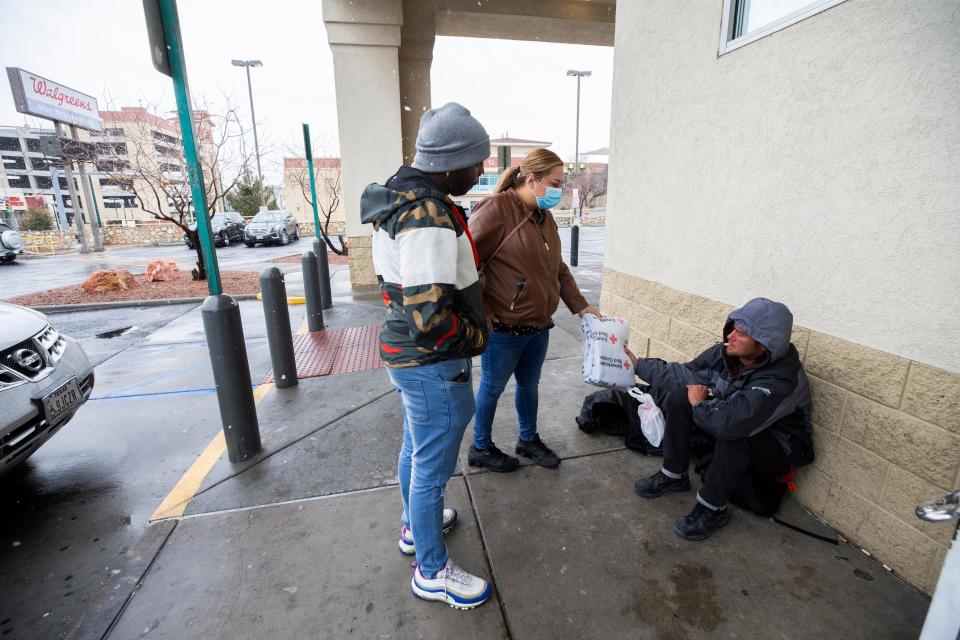 Opportunity Center for the Homeless outreach leads Lawrence Miller and Nichol Torres hand out a blanket from the Red Cross to a homeless man as rain and snow fell Friday in El Paso.