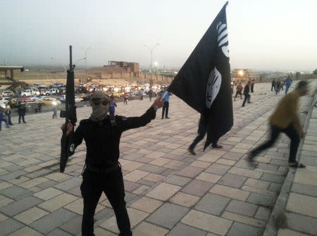 A fighter of the Islamic State of Iraq and the Levant (ISIL) holds an ISIL flag and a weapon on a street in the city of Mosul, June 23, 2014. REUTERS/Stringer