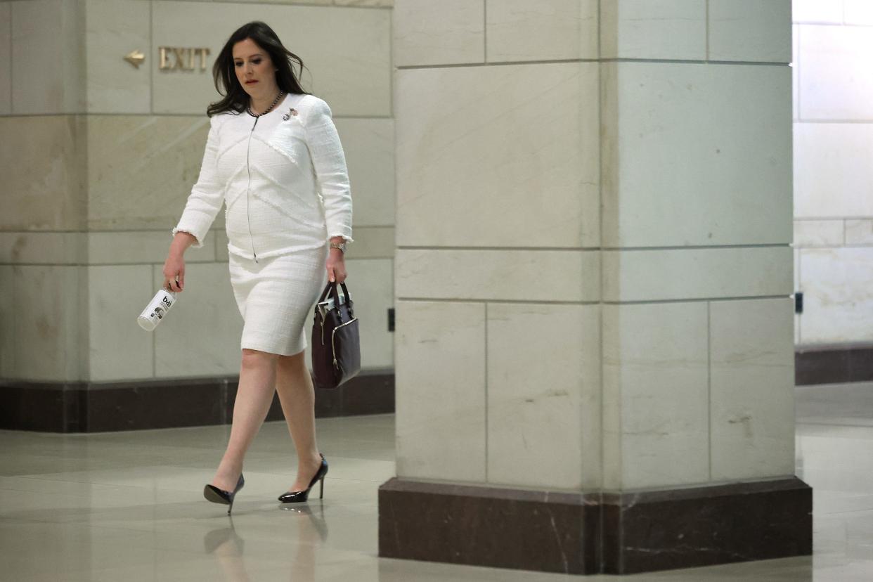 Elise Stefanik walks through the halls of the US Capitol holding a bag and drink in both hands.