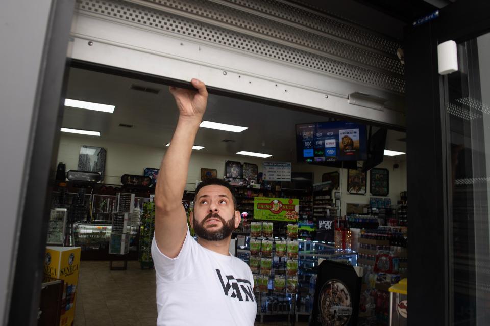 George Touma, co-owner of House of Smokes in Ventura with his brother Nadim Touma, rolls up a security door on Tuesday. The brothers have added new security measures over the years after a number of break-ins.