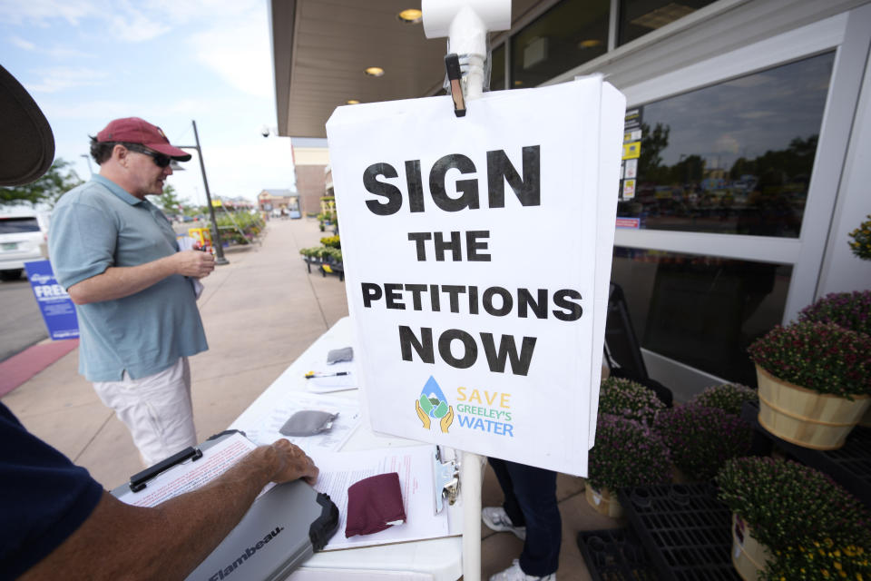 In this Friday, July 223, 2021, photograph, a passer-by stops at a stand set up by John G. Gauthiere, president of his own civil engineering consulting firm, to collect signatures outside a grocery store in west Greeley, Colo. Figures released this month show that population growth continues unabated in the South and West, even as temperatures rise and droughts become more common. That in turn has set off a scramble of growing intensity in places like Greeley to find water for the current population, let alone those expected to arrive in coming years. (AP Photo/David Zalubowski)