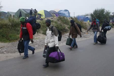 Migrants with their belongings walk past tents at the start of their evacuation and transfer to reception centers in France, and the dismantlement of the camp called the "Jungle" in Calais, France, October 24, 2016. REUTERS/Pascal Rossignol