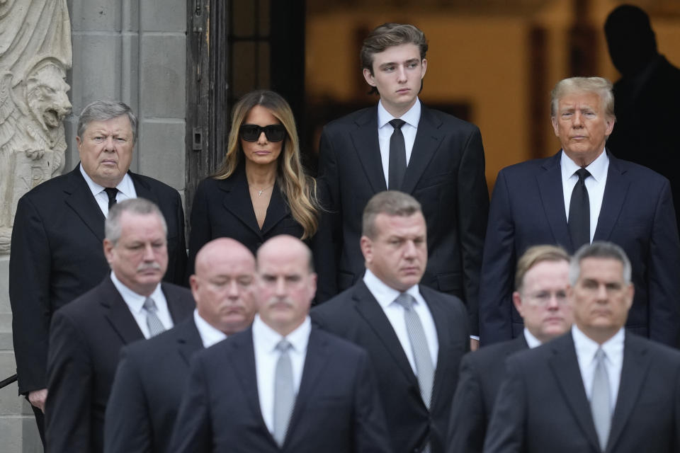 Former President Donald Trump, right, stands with his wife Melania, second left, their son Barron, center, and father-in-law Viktor Knavs, left, as pallbearers walk to receive the coffin carrying the remains of Amalija Knavs, the former first lady's mother, is carried into the Church of Bethesda-by-the-Sea for her funeral, in Palm Beach, Fla., Thursday, Jan. 18, 2024. (AP Photo/Rebecca Blackwell)