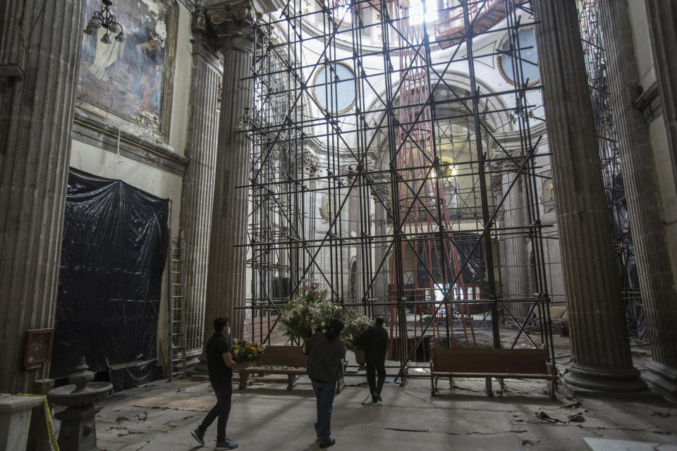 Scaffolding supports the interior of the quake-damaged Our Lady of the Angels Catholic Church, as parishioners carry off flowers that had adorned a painting of the Assumption of the Virgin to be offered to faithful, in Mexico City, Sunday, Aug. 7, 2022. The National Institute of Anthropology and History, who is funding and carrying out the restoration project, began work on the temple in September 2019, two years after the Sept. 19, 2017 quake. Phase one involved stabilizing the structure with steel supports to prevent further loss, and covering the collapsed dome to keep out rainwater. That ended in December 2020, and since then it has been a long wait for phase two, which began Aug. 8. (AP Photo/Ginnette Riquelme)