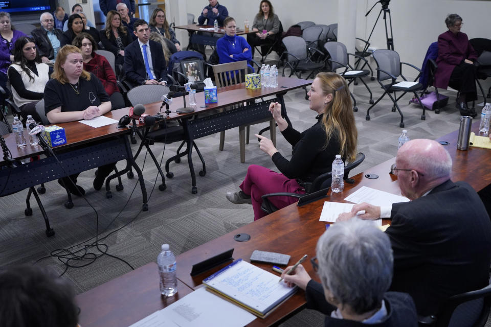 Megan Vozzella, seated at table on left, watches sign language interpreter Grace Cooney, seated in front of table at right, during a hearing of the independent commission investigating the law enforcement response to the mass shooting in Lewiston, Maine, Thursday, Feb. 1, 2024, in Augusta, Maine. Maine's deaf community recovering from the loss of several deaf people in the mass shooting.(AP Photo/Robert F. Bukaty)