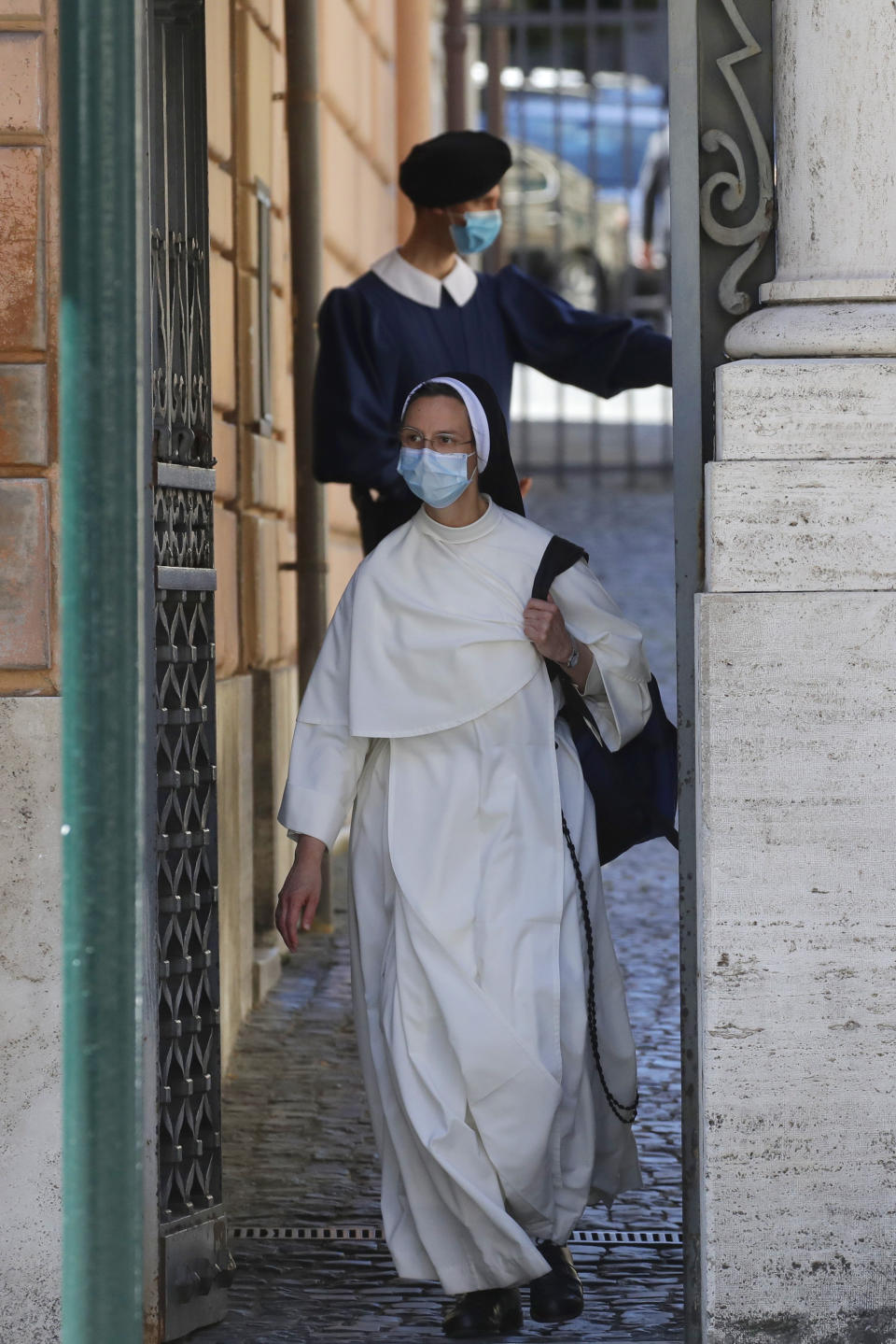 A nun passes by a Swiss Guard as she leaves the Vatican Monday, May 4, 2020. The Vatican is postponing the annual swearing-in ceremony for its new crop of Swiss Guards, a commemoration usually held each May 6 to honor the guardsmen who died while protecting the pope during the 1527 Sack of Rome. The Swiss Guards said Monday that due to the ongoing coronavirus emergency, the pomp-filled ceremony will now be held Oct. 4. (AP Photo/Alessandra Tarantino)