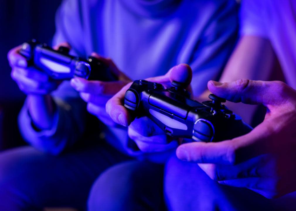 Two people playing video games in a room under blue light from a television.