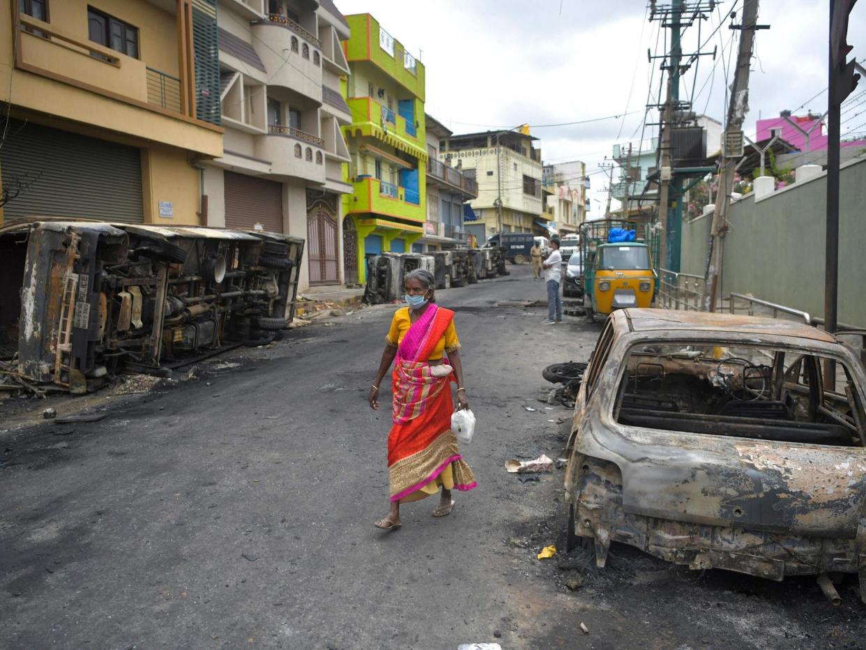 A resident walks past the burned-out remains of a car following protests in the city of Bengaluru, India, over a Facebook post about the Prophet Mohammed: Manjunath Kira/Getty