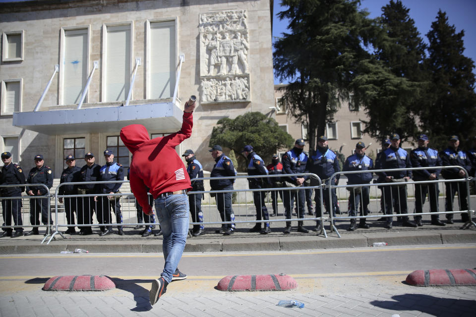 A protester throws a smoke bomb at police guarding the government building as thousands of opposition supporters protest in Tirana, Albania on Saturday, March 16, 2019. Albanian opposition supporters clashed with police while trying to storm the parliament building Saturday in a protest against the government which they accuse of being corrupt and linked to organized crime.(AP Photo/Visar Kryeziu)