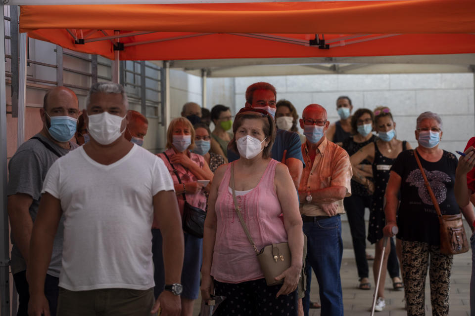 People wearing face masks queue up to be tested for COVID-19, outside a local clinic in Santa Coloma de Gramanet in Barcelona, Spain, Tuesday, Aug. 11, 2020. Spain is facing another surge in coronavirus infections not even two months after beating back the first wave. (AP Photo/Emilio Morenatti)