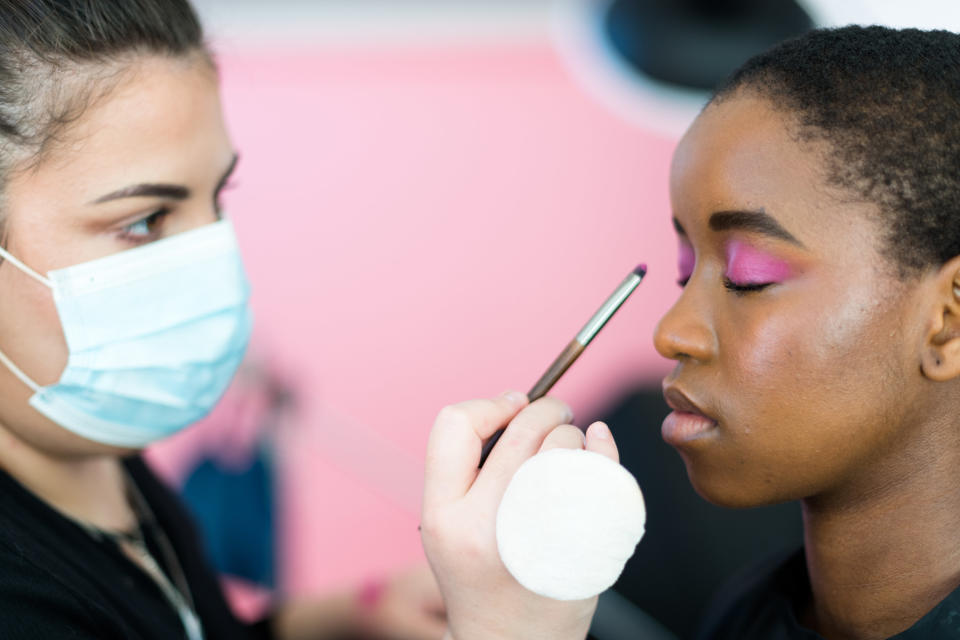 Makeup artist in a surgical mask applying eyeshadow to a model