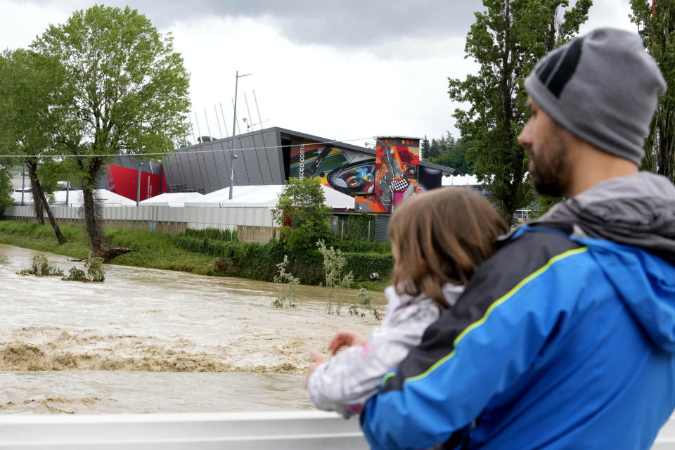 A man holding a child looks at the swollen Santerno River with behind the Enzo e Dino Ferrari circuit, in Imola, Italy, Wednesday, May 17, 2023. The weekend's Emilia-Romagna Grand Prix in Imola has been canceled because of deadly floods. Formula One said it made the decision for safety reasons and to avoid any extra burden on the emergency services. F1 personnel had earlier been told to stay away from the track after floods affected large parts of the Emilia-Romagna region. (AP Photo/Luca Bruno)