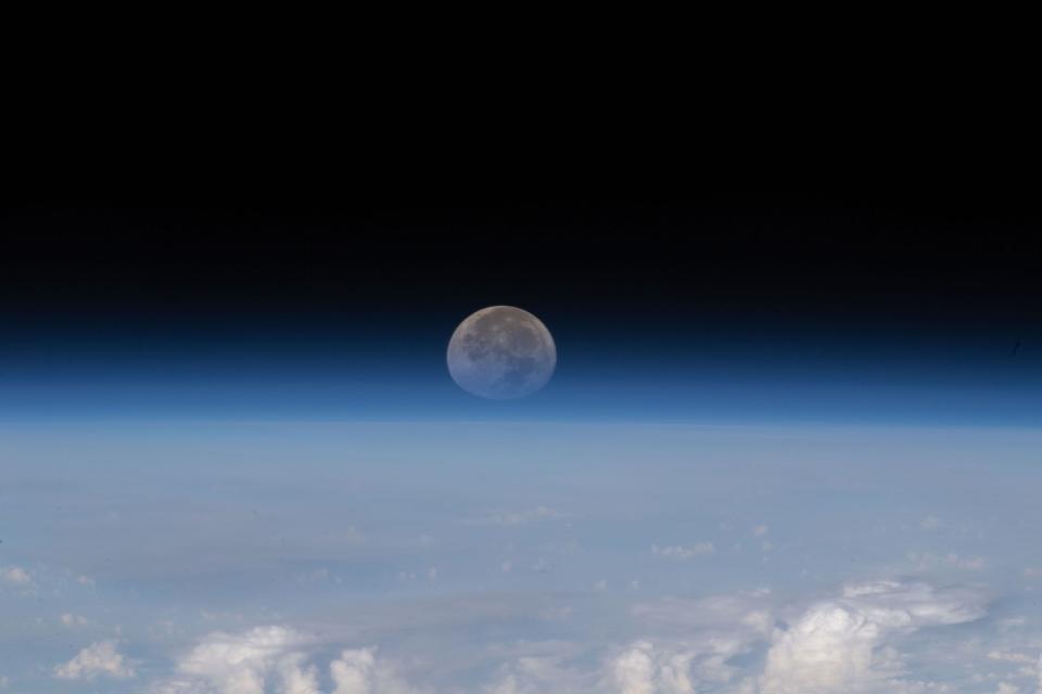 moon sets below earth horizon against blackness of space
